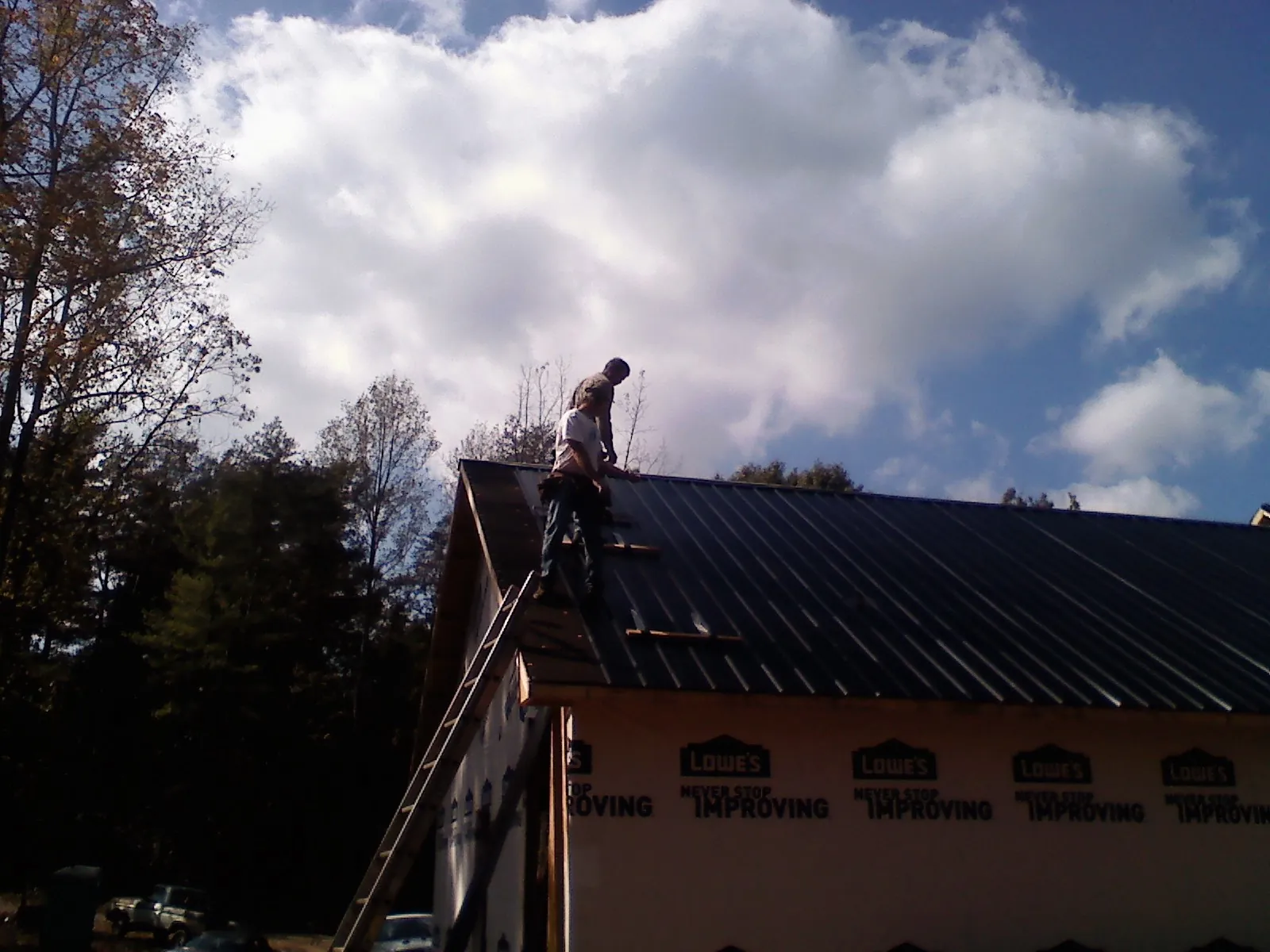 Roofer fastening dark metal panels high against a cloudy sky, from a Roof Inspection job in Old Hickory