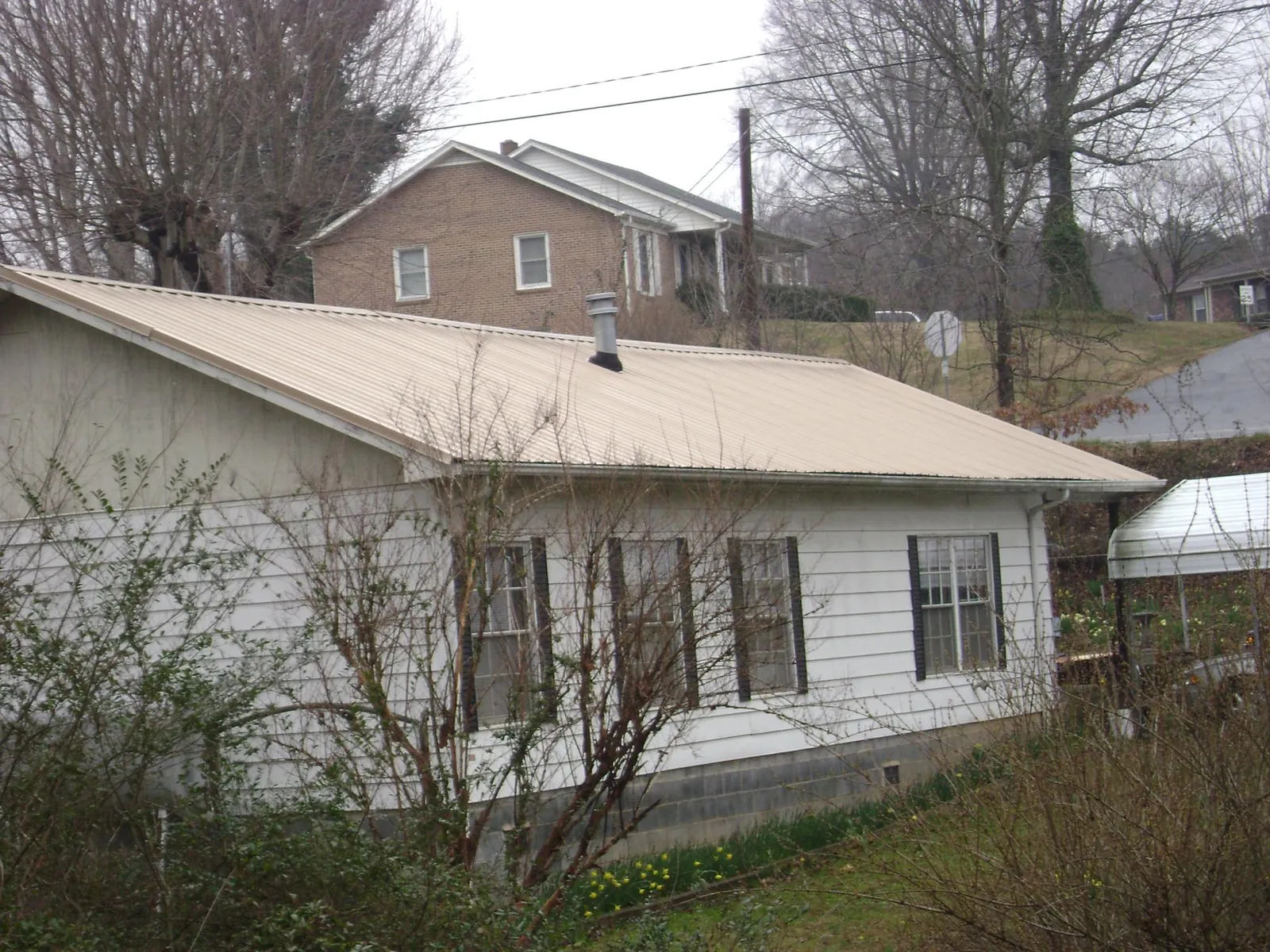Tan metal roof on a white sided house set into a hillside — Commercial Roofing by Roofing Brothers in Old Hickory